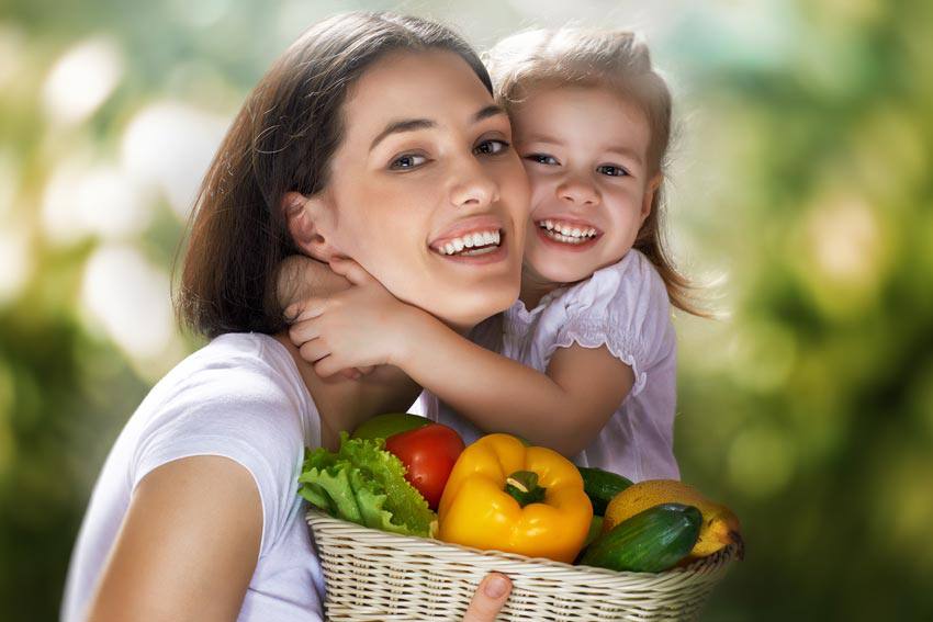 A mother with her daughter holding a basket of fresh vegetables