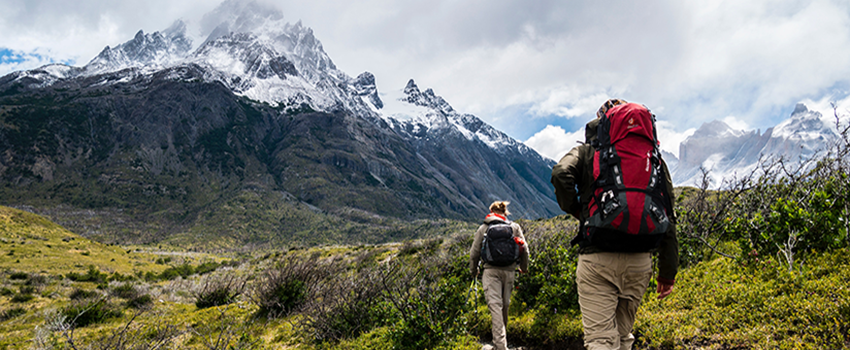 Two people hiking beside a mountain on a trail