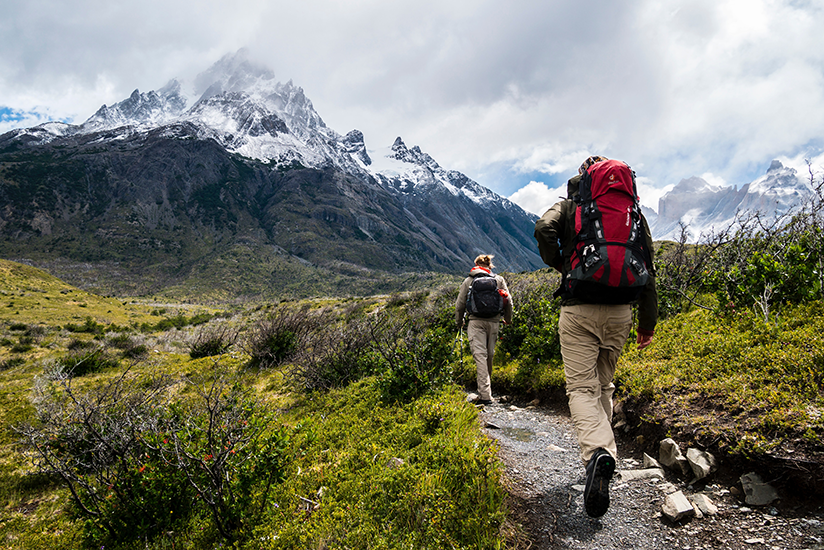 Two people hiking beside a mountain on a trail