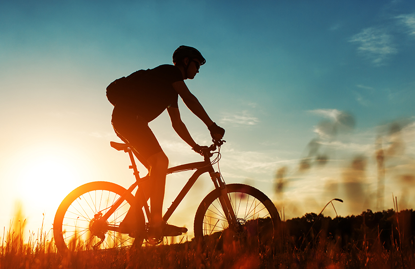 A person cycling in front the sunset in a field