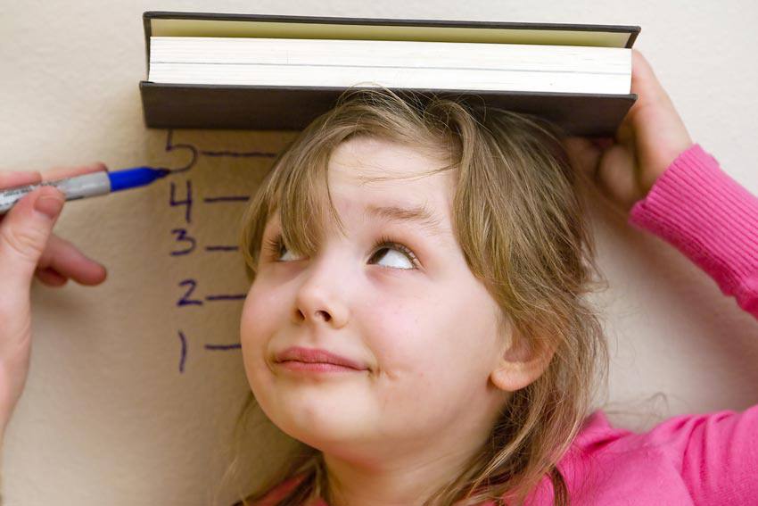 A child measuring their height using a book and a pen