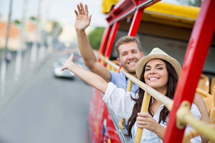 Two tourists waving their hand out of a tour bus