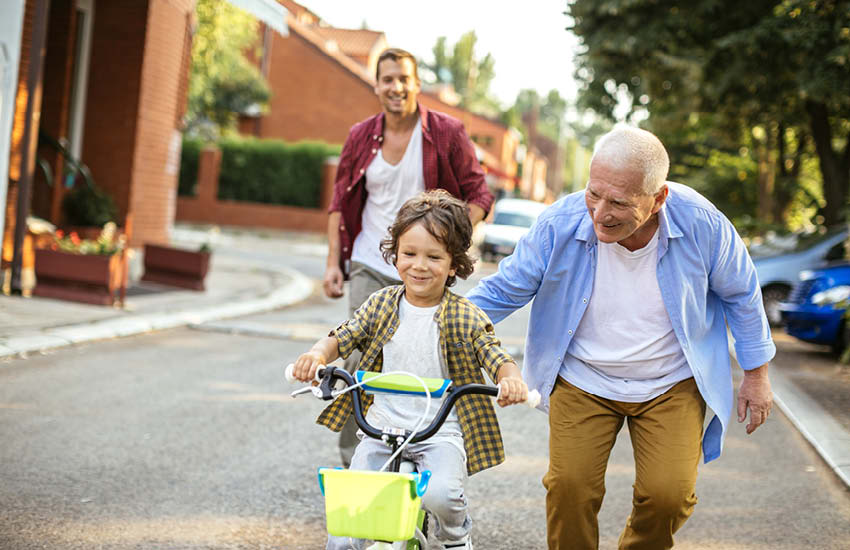 An elderly man teaching his grandson how to ride a bike