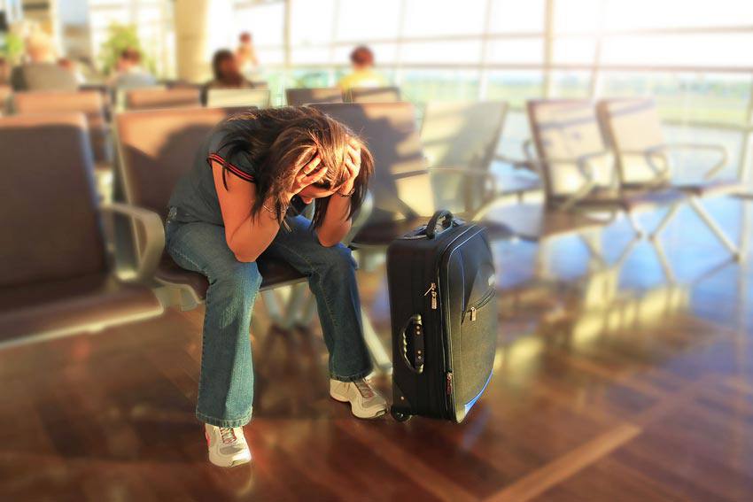 A woman sitting at the airport with their hands on their head 