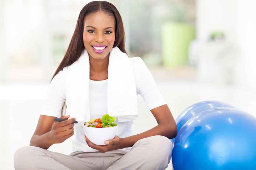 A woman eating a salad beside an exercise ball