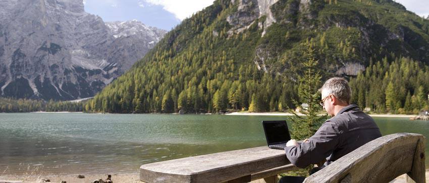 A man sitting on a bench using a computer beside a lake 